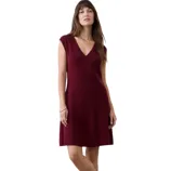 A woman is wearing a burgundy V-neck sleeveless dress paired with black loafers, standing against a neutral background.