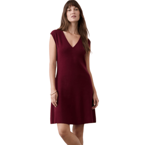 A woman is wearing a burgundy V-neck sleeveless dress paired with black loafers, standing against a neutral background.