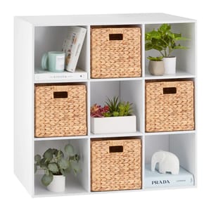 White cube organizer featuring five wicker baskets, various books, and decorative items like potted plants, a white elephant figurine, and a small succulent arrangement.