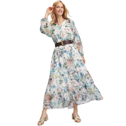 A woman is wearing a floral maxi dress with long sleeves, paired with a wide brown belt and beige slide sandals.