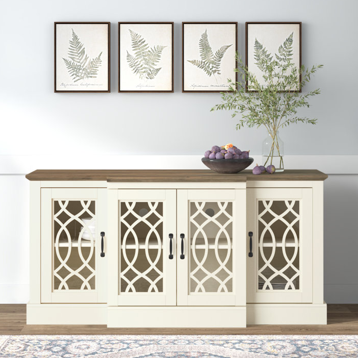 A sideboard with decorative cabinet doors and a wooden countertop, accompanied by framed fern prints on the wall and a vase with greenery.