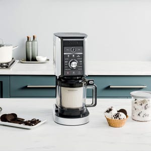 A Ninja coffee maker stands on a kitchen counter next to a plate of cookies and a bowl of ice cream.