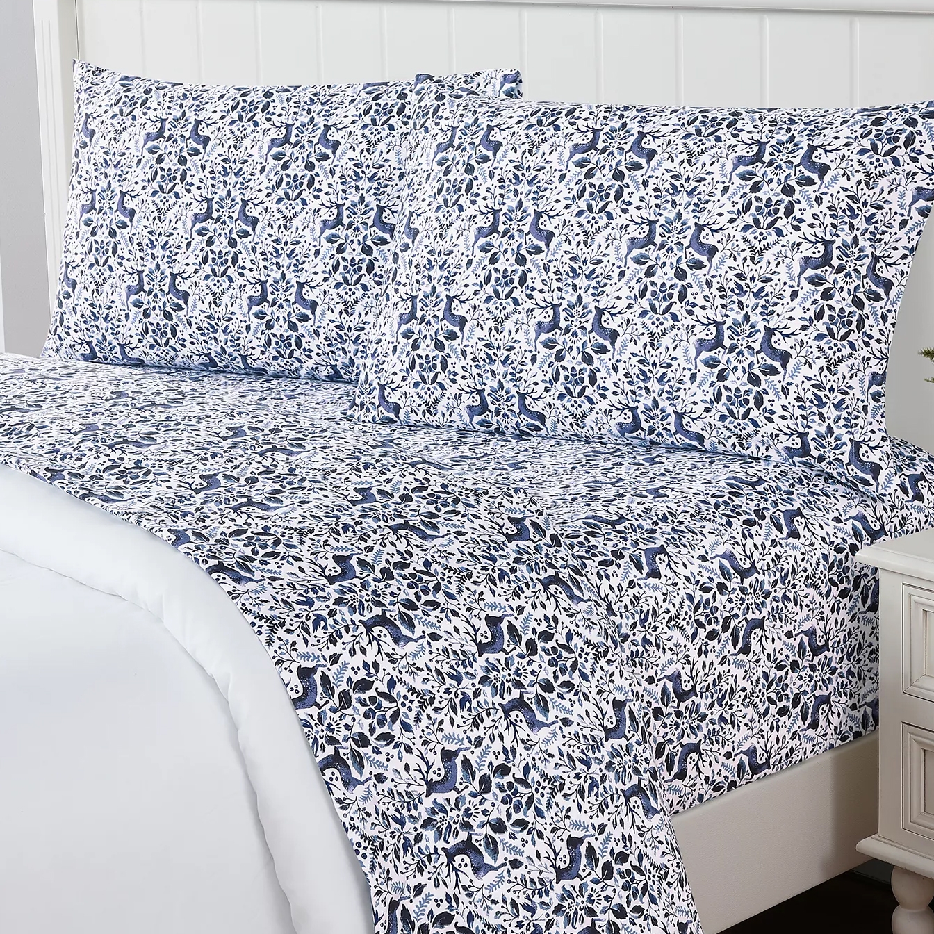 A patterned bedsheet set featuring a blue and white botanical and animal design on a bed with matching pillowcases.