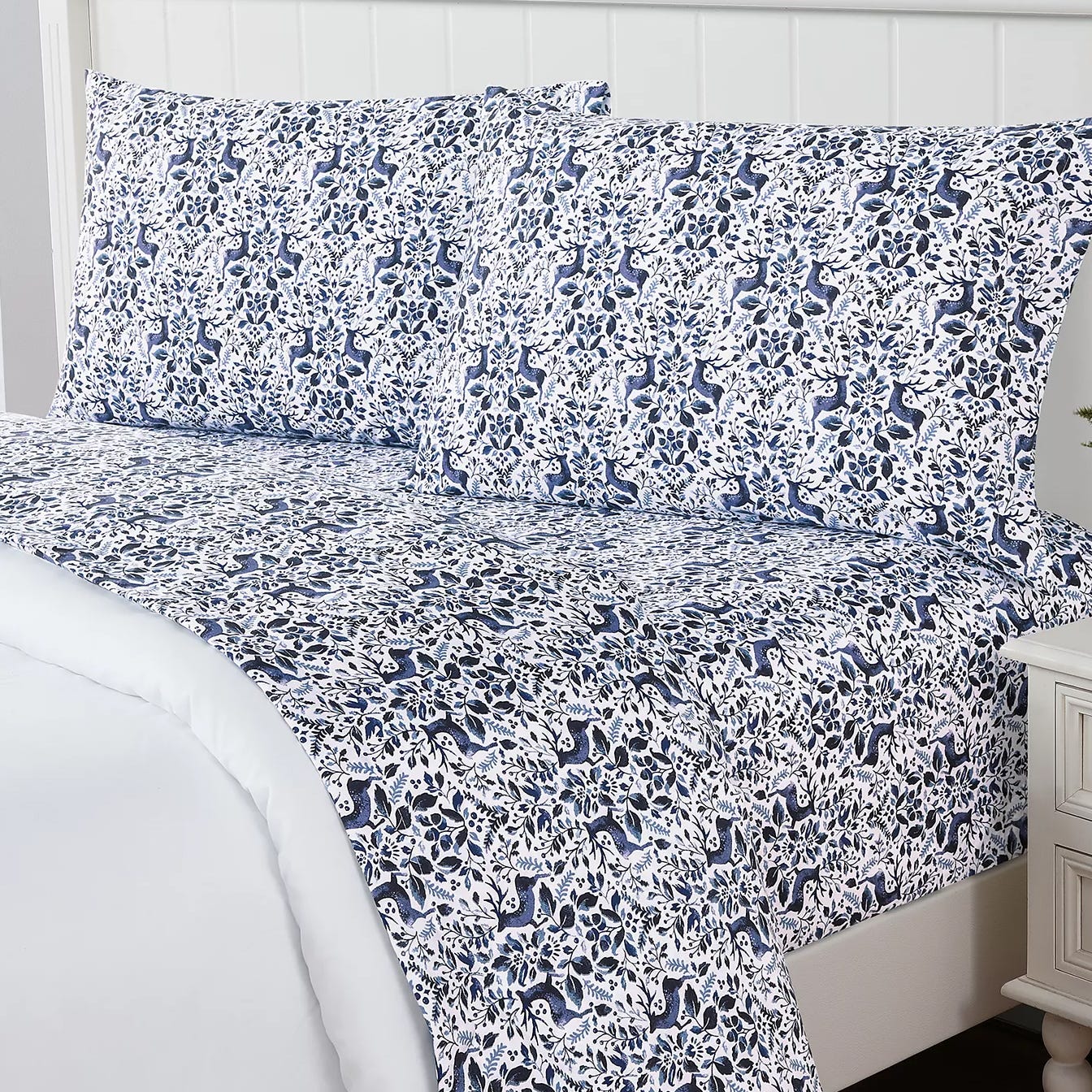 A patterned bedsheet set featuring a blue and white botanical and animal design on a bed with matching pillowcases.