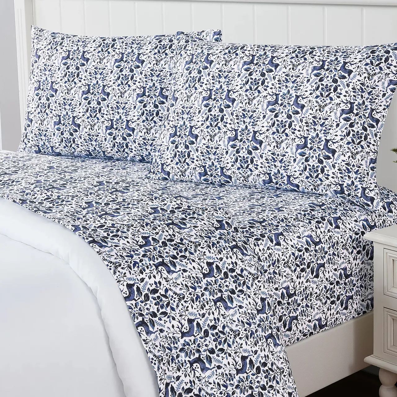 A patterned bedsheet set featuring a blue and white botanical and animal design on a bed with matching pillowcases.
