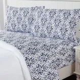 A patterned bedsheet set featuring a blue and white botanical and animal design on a bed with matching pillowcases.