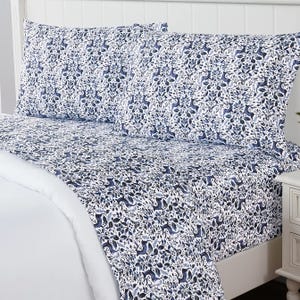 A patterned bedsheet set featuring a blue and white botanical and animal design on a bed with matching pillowcases.