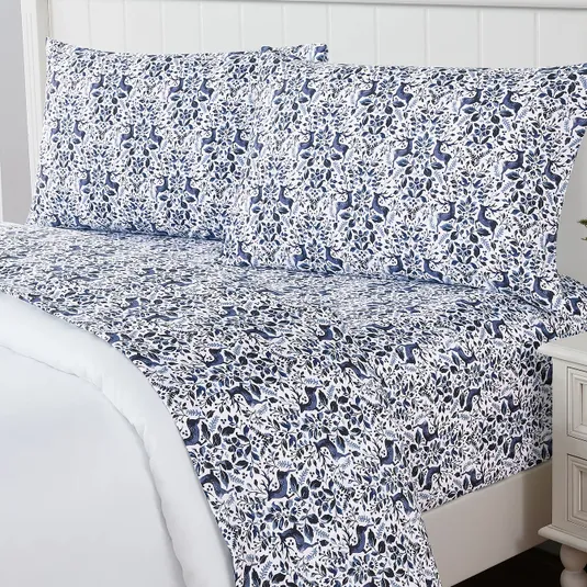 A patterned bedsheet set featuring a blue and white botanical and animal design on a bed with matching pillowcases.