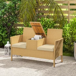 A wicker outdoor loveseat with beige cushions features a storage compartment between the seats. It's set in a garden with lush greenery and accompanied by decorative lanterns on the ground.