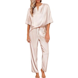 Women's satin pajamas in a light cream color, featuring a loose-fitting top with short sleeves and a round neckline, paired with matching drawstring pants.