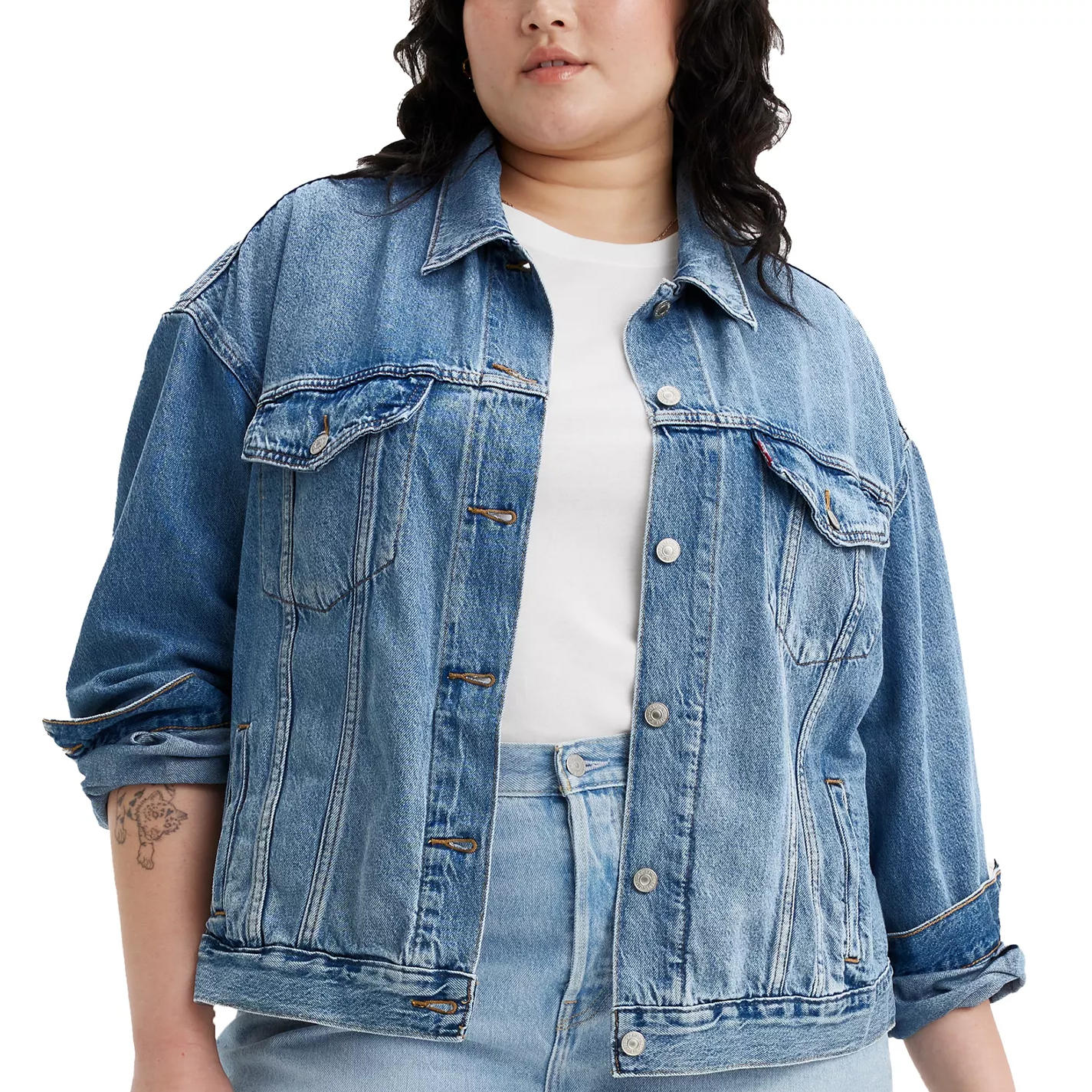 A person wearing a blue denim jacket over a white shirt and light blue jeans, with rolled-up sleeves.