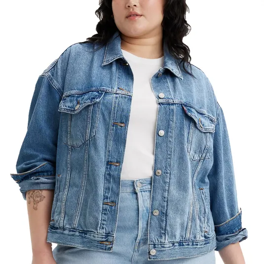 A person wearing a blue denim jacket over a white shirt and light blue jeans, with rolled-up sleeves.