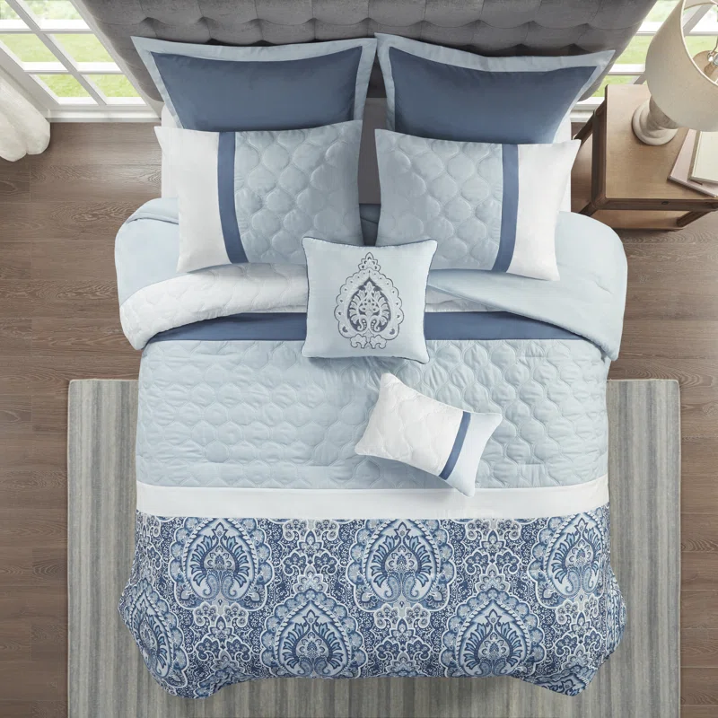 A bedding set with blue and white pillows, comforter, and quilt with paisley designs.