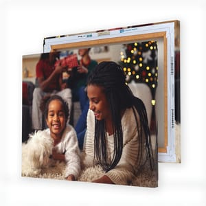 A framed canvas print featuring a joyful scene with two people and a white dog, against a festive background with a Christmas tree.
