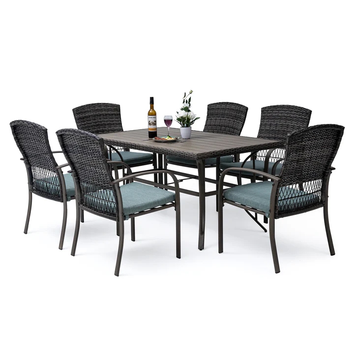 Outdoor dining furniture set with a rectangular table, six wicker chairs with blue cushions, and a bottle with two glasses on the table.