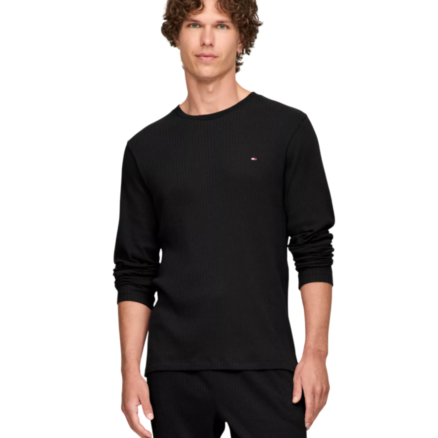 A man wears a black long-sleeve ribbed shirt with a small logo on the chest and matching black pants.