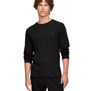 A man wears a black long-sleeve ribbed shirt with a small logo on the chest and matching black pants.