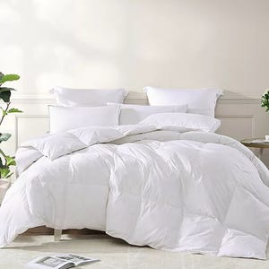 A plush white comforter filled with goose feathers, featuring a quilted design and accompanied by matching white pillows, offers a cozy and luxurious bedding setup.
