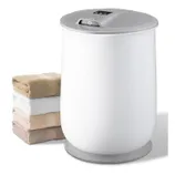 A white electronic towel warmer with a gray lid is shown next to a neatly stacked set of four folded towels in various neutral colors.