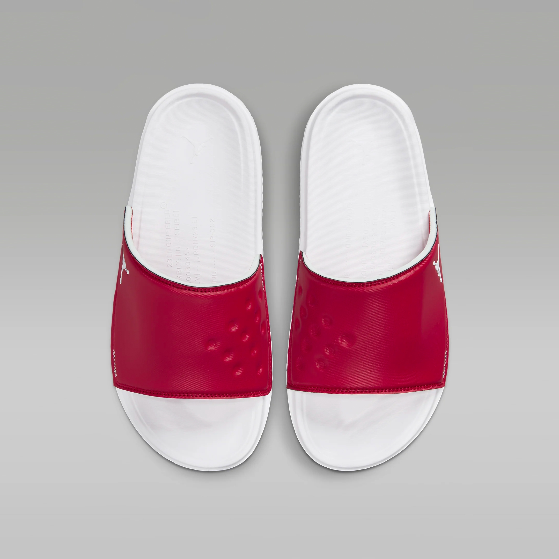 A pair of red and white slide sandals with a contoured footbed and logo detail.