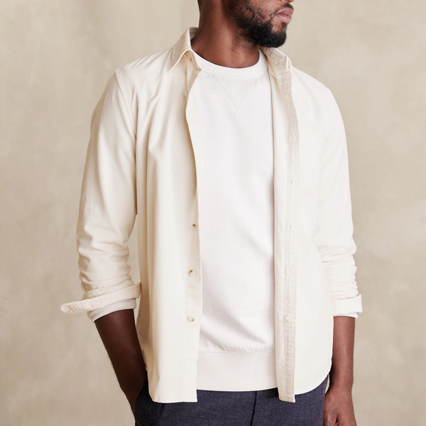 A man wearing a cream-colored button-up shirt over a white long-sleeve t-shirt paired with dark trousers.