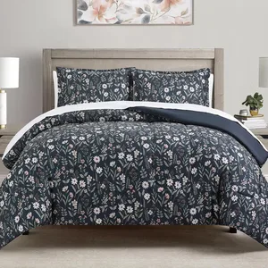 A bed features a floral-patterned comforter and pillow shams in dark tones with white flowers. The bedding is complemented by a wooden headboard, bedside tables with lamps, and a floral wall art piece above the bed.