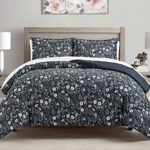 A bed features a floral-patterned comforter and pillow shams in dark tones with white flowers. The bedding is complemented by a wooden headboard, bedside tables with lamps, and a floral wall art piece above the bed.