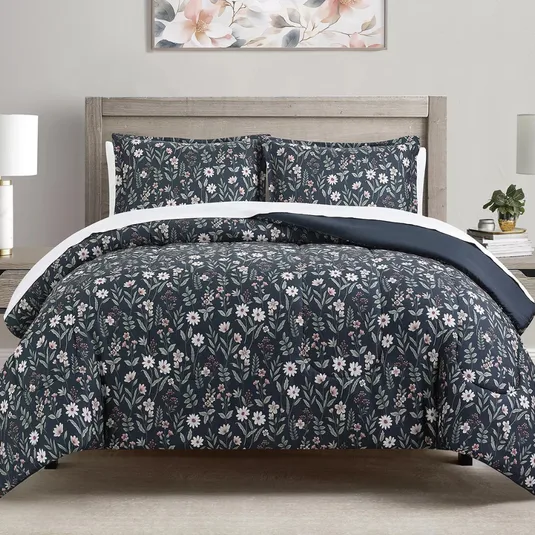 A bed features a floral-patterned comforter and pillow shams in dark tones with white flowers. The bedding is complemented by a wooden headboard, bedside tables with lamps, and a floral wall art piece above the bed.