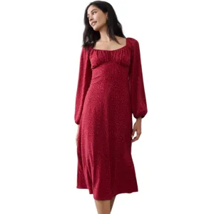 A woman is wearing a red, long-sleeve, mid-length dress with a square neckline and a subtle pattern. She pairs it with black ankle boots.