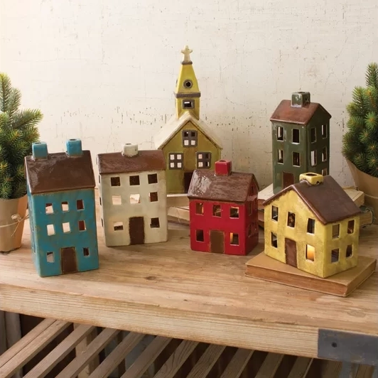 A set of six miniature, festive-colored houses and a church, designed as holiday decorations with light-up windows. Some are accented with faux snow and greenery.