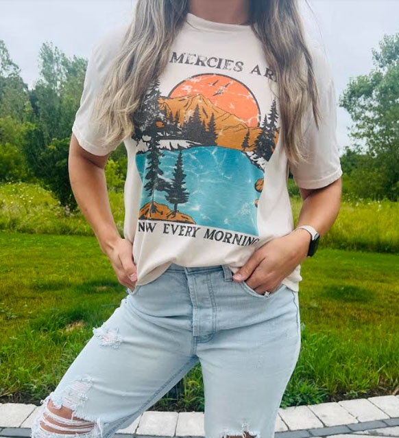 A person is wearing a graphic t-shirt with a nature scene and light blue ripped jeans.
