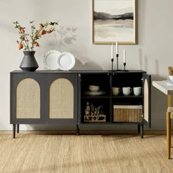 A dark wood sideboard with wicker doors stands on a woven rug, featuring open shelves displaying plates and mugs. A vase with branches, decorative plates, and candlesticks adorn the top, with a framed abstract artwork hanging above.