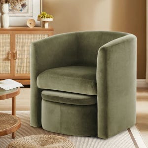 Green upholstered barrel chair with a curved backrest, situated in a cozy room with a wooden cabinet and round table.