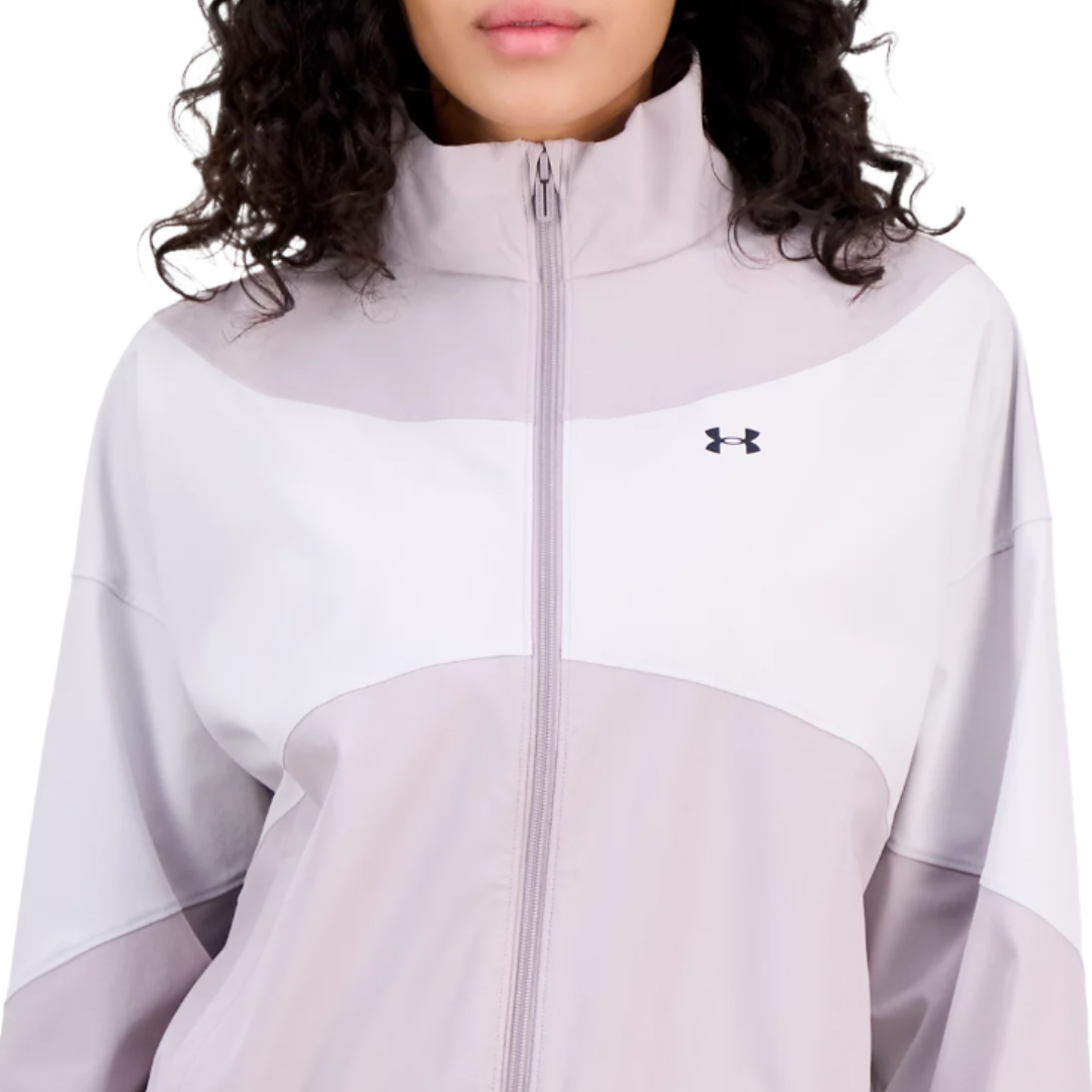 A woman is wearing a light purple and white Under Armour jacket with a high collar and zip closure, featuring the Under Armour logo on the chest.