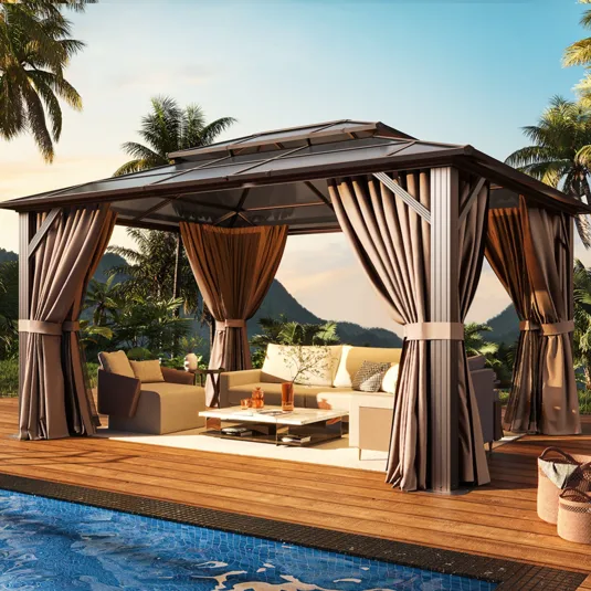 A gazebo with draped curtains and a seating area is set on a wooden deck beside a pool, surrounded by tropical plants and mountains in the background.