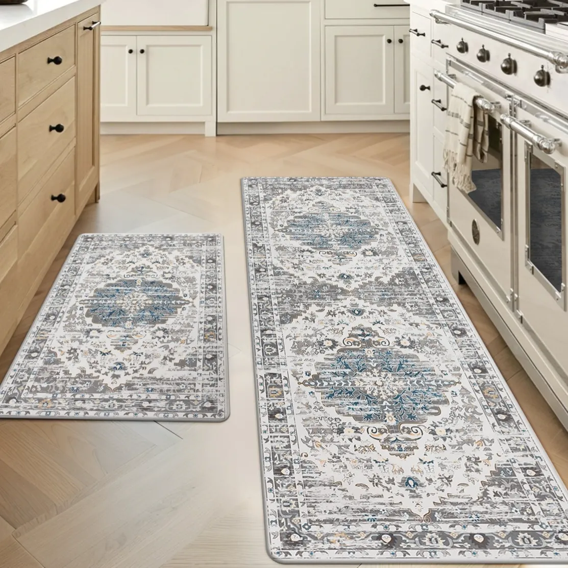 Two kitchen rugs with intricate blue and gray patterns are placed on a light wooden floor, adjacent to wooden cabinets and a white stove.