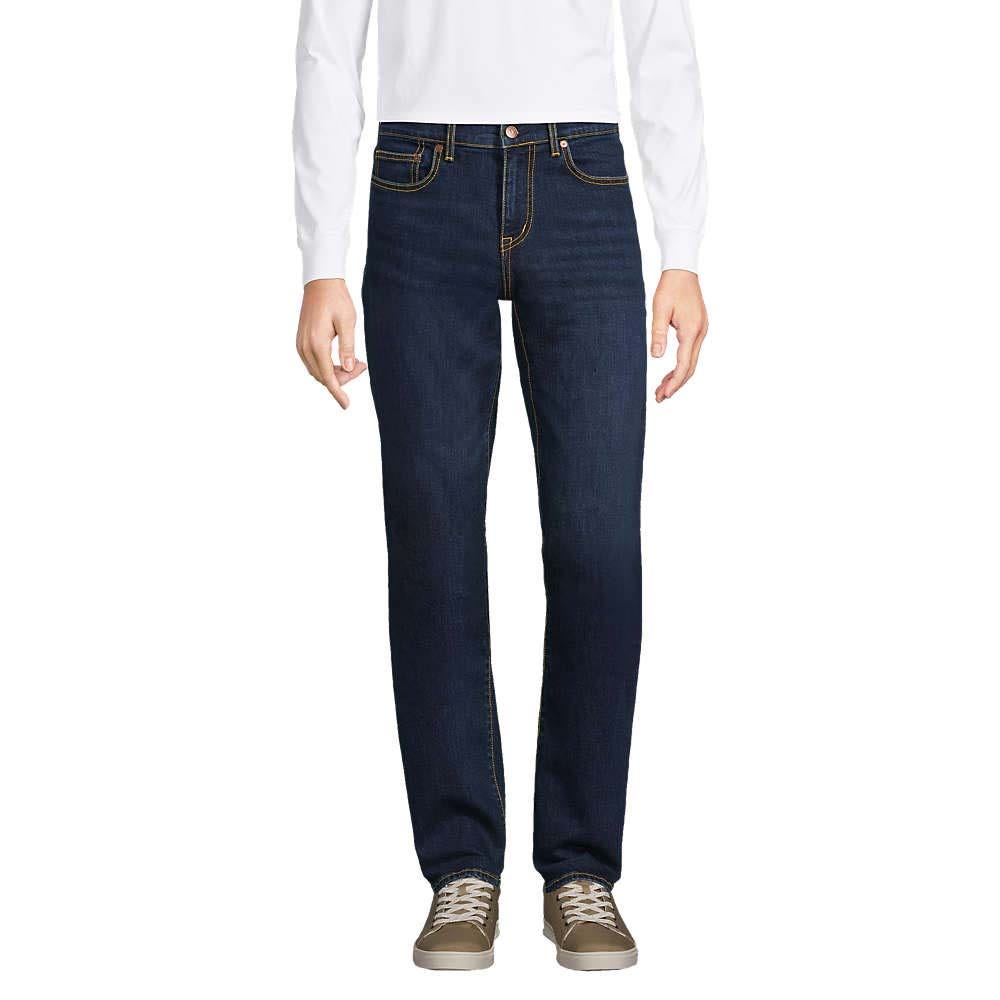 A person wearing dark blue straight-leg jeans with contrast stitching, paired with a white long-sleeve shirt and brown sneakers.