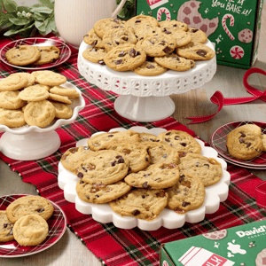 An arrangement of cookies on decorative stands and plates set on a red plaid tablecloth, next to a festive green box with holiday designs, possibly from David's Cookies.
