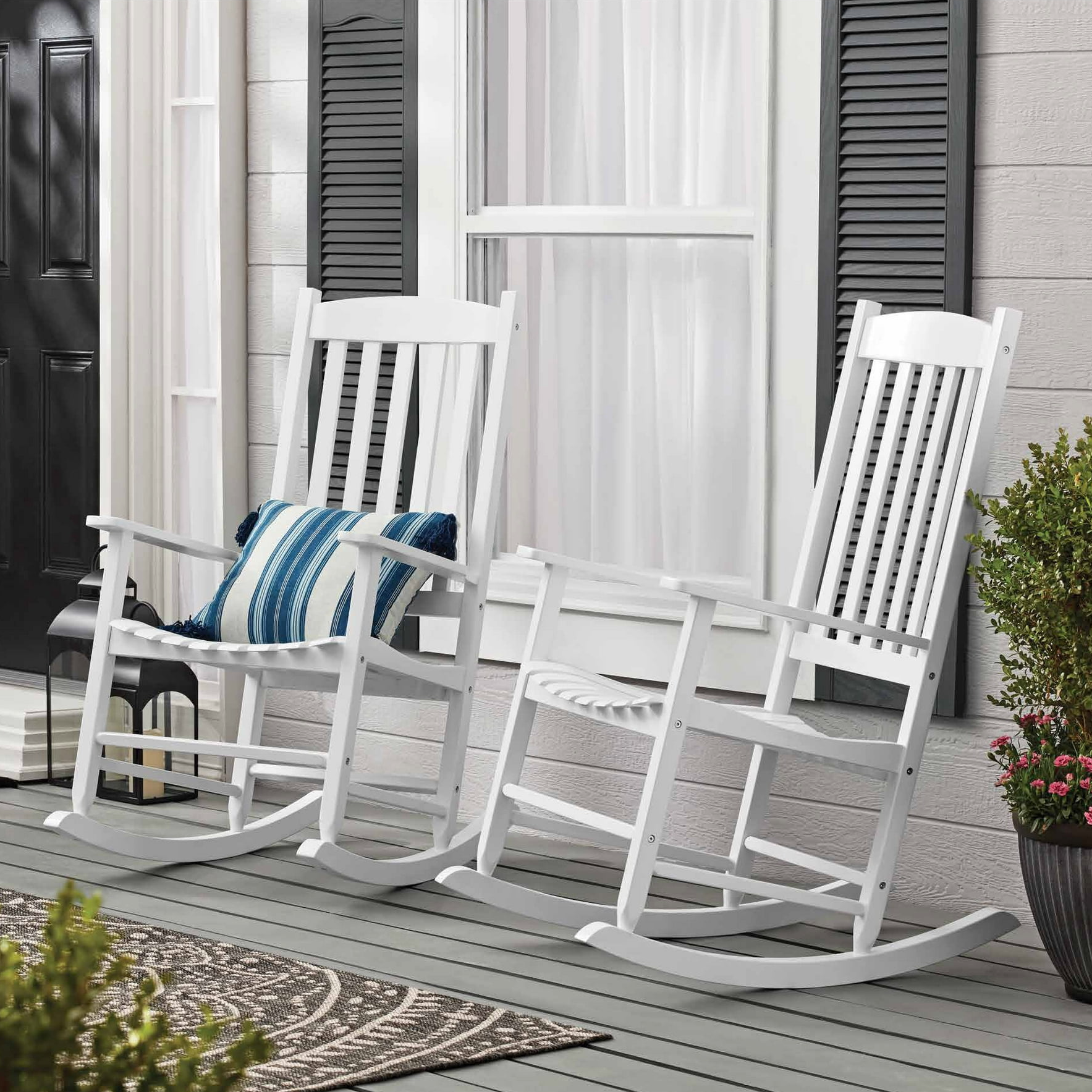 Two white rocking chairs on a porch with a blue striped cushion on one of them.