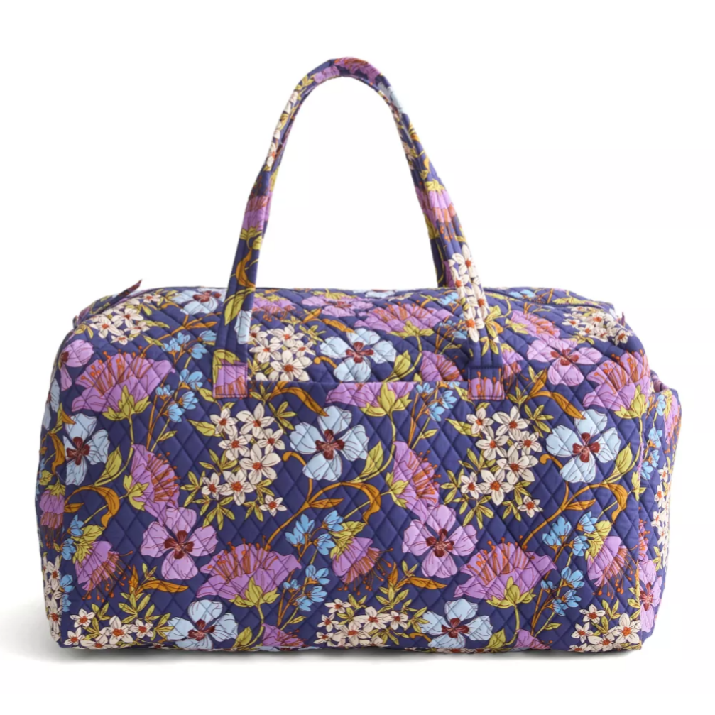 Quilted fabric weekender bag featuring a vibrant floral pattern with purple, white, and blue flowers on a dark background, equipped with two handles.