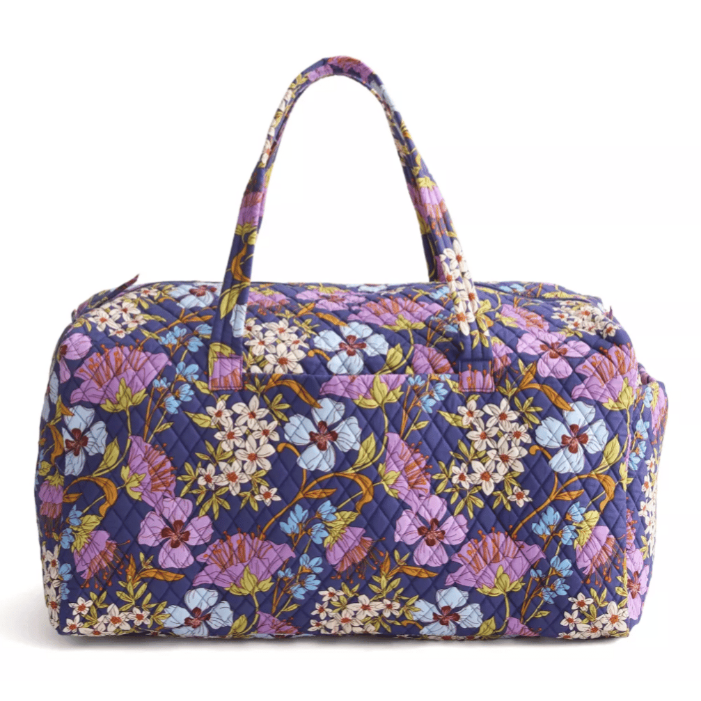 Quilted fabric weekender bag featuring a vibrant floral pattern with purple, white, and blue flowers on a dark background, equipped with two handles.
