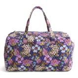 Quilted fabric weekender bag featuring a vibrant floral pattern with purple, white, and blue flowers on a dark background, equipped with two handles.