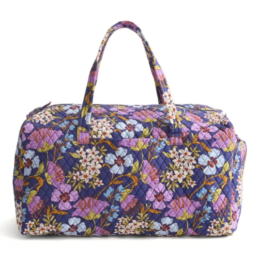 Quilted fabric weekender bag featuring a vibrant floral pattern with purple, white, and blue flowers on a dark background, equipped with two handles.