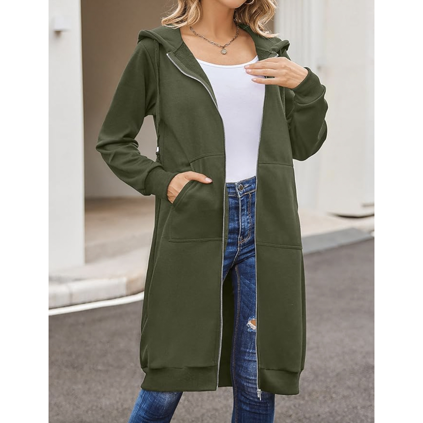 Woman wearing a long green hoodie with a zipper, paired with blue jeans and a white top.