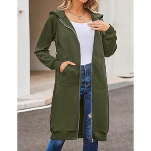 Woman wearing a long green hoodie with a zipper, paired with blue jeans and a white top.