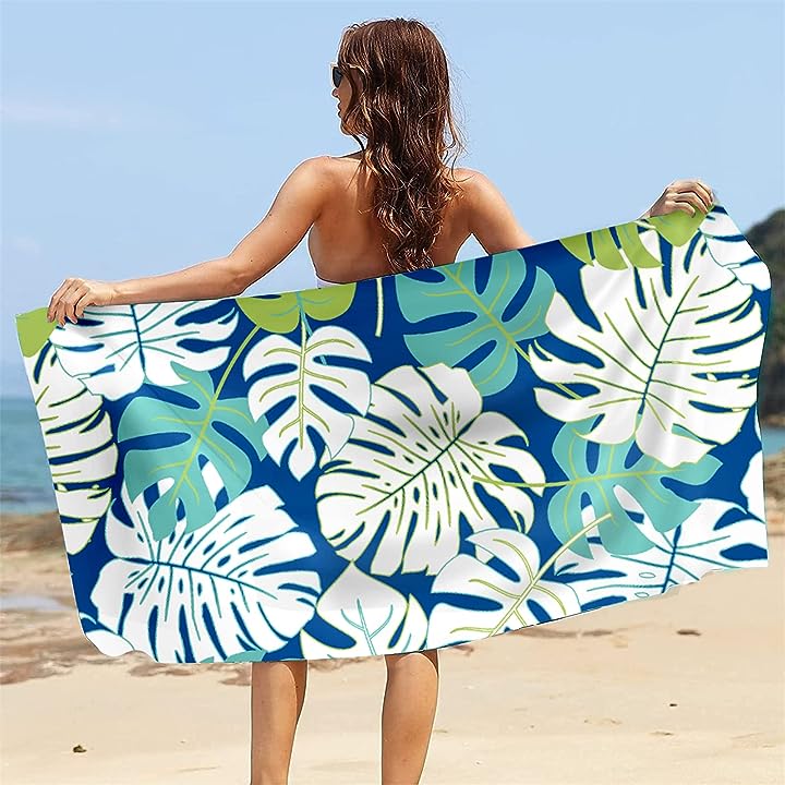 A woman is holding a large, blue and green, leaf-patterned beach towel.