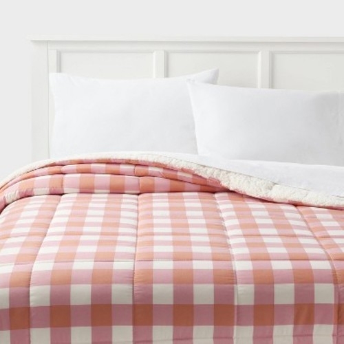 A bed is made with a pink and white checkered comforter, complemented by white pillows and a white headboard.