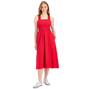 A woman is wearing a knee-length red dress with a smocked bodice, wide straps, and pockets. She pairs it with white sneakers.