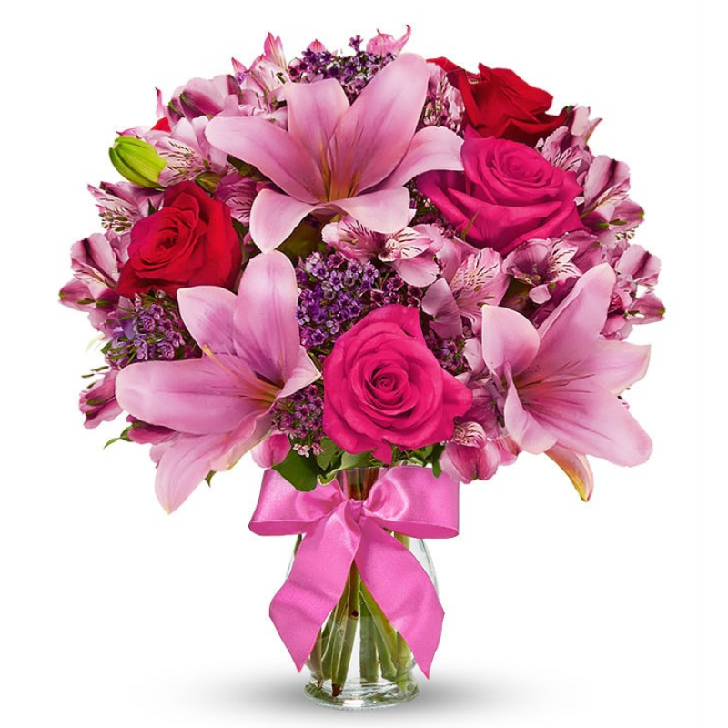 A vibrant bouquet featuring pink lilies, hot pink and red roses, and accent flowers in a clear vase with a pink ribbon.