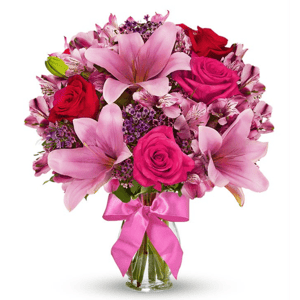 A vibrant bouquet featuring pink lilies, hot pink and red roses, and accent flowers in a clear vase with a pink ribbon.
